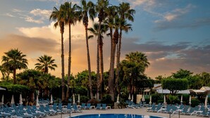 A pool area with lounge chairs and palm trees. - AQUA Hotel Aquamarina & Spa (Santa Susanna)