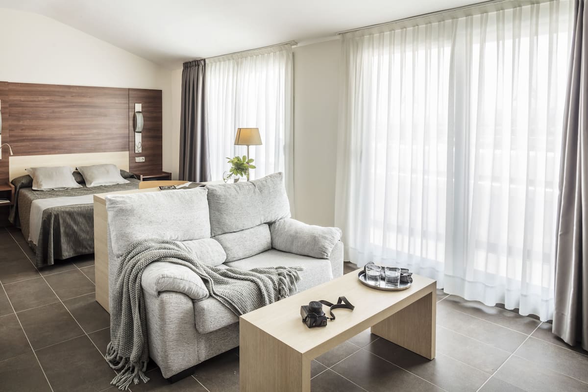 Una habitación de hotel moderna con sofá, una mesita, lámpara y cama.