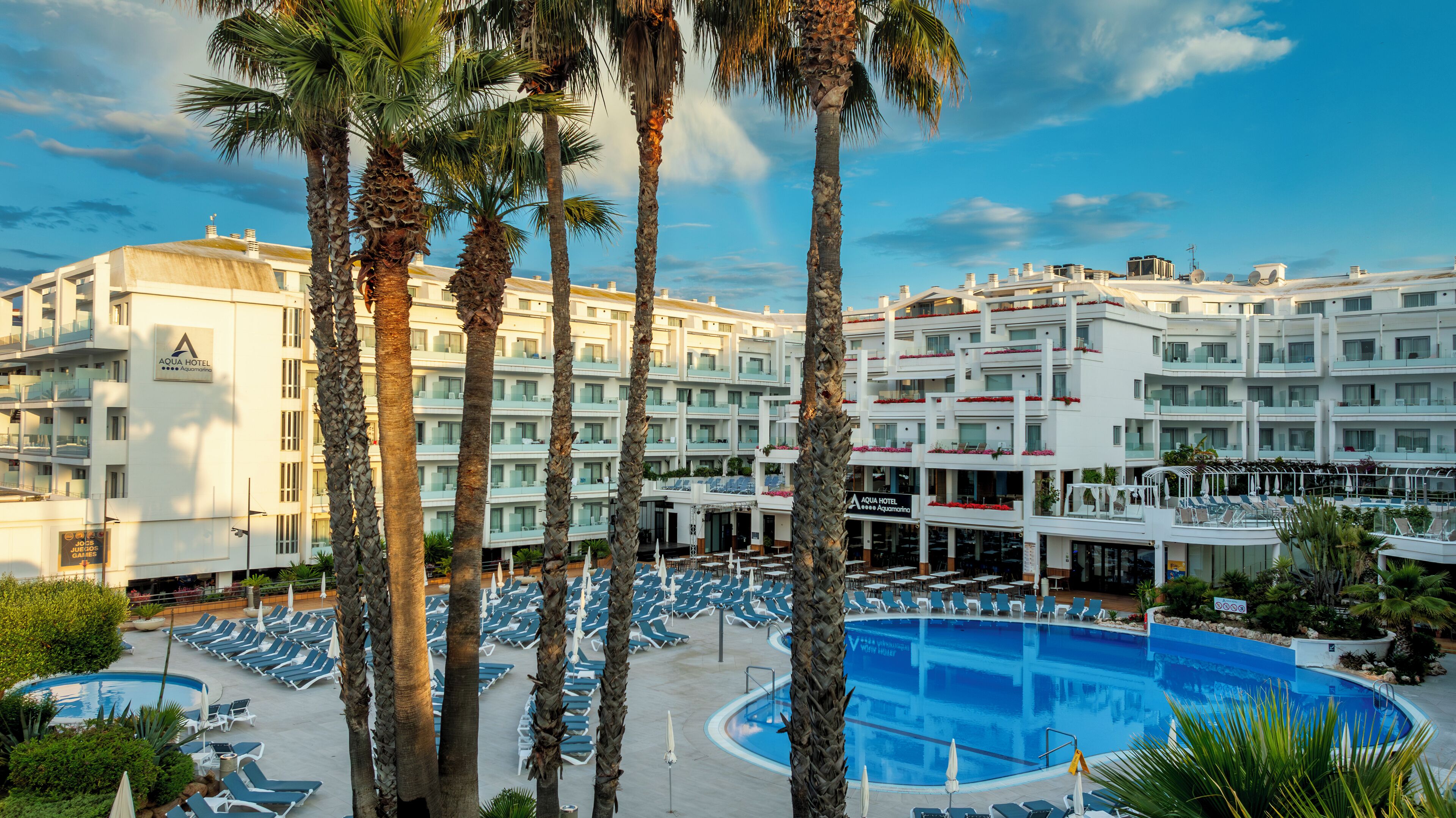 Un hotel con piscina rodeado de palmeras y tumbonas.