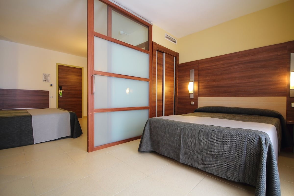 Habitación de hotel con dos camas, una puerta corredera y un cabecero de madera.