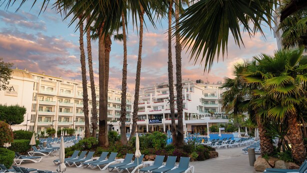 A hotel with a pool area, sun loungers, palm trees, and a building with multiple balconies. - AQUA Hotel Aquamarina & Spa (Santa Susanna)