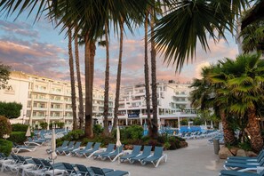 A hotel with a pool area, sun loungers, palm trees, and a building with multiple balconies. - AQUA Hotel Aquamarina & Spa (Santa Susanna)
