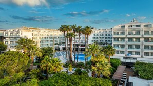 A hotel with multiple floors, a swimming pool surrounded by palm trees, and a Burger Club sign. - AQUA Hotel Aquamarina & Spa (Santa Susanna)