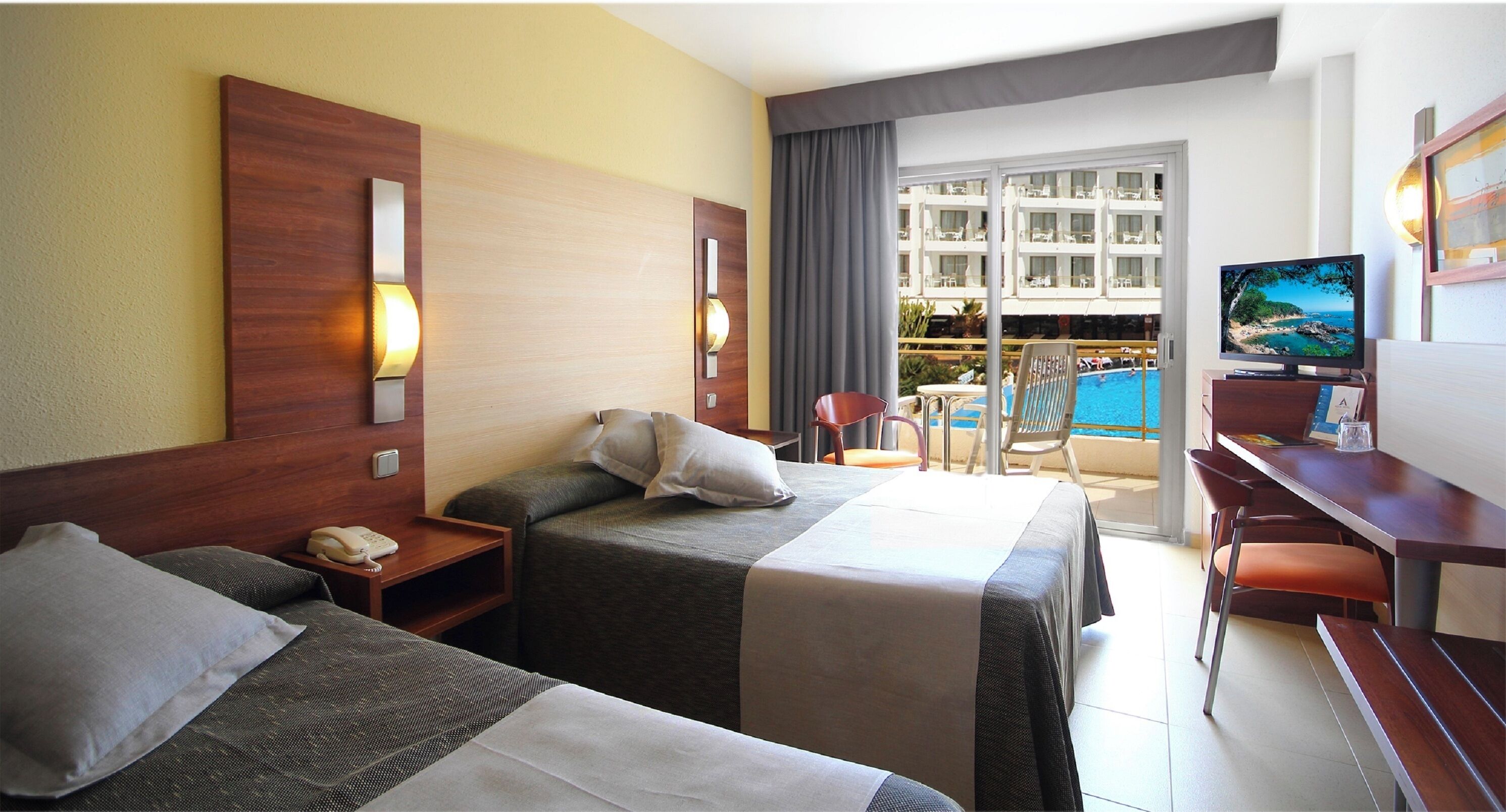 A hotel room with two beds, a desk, a TV, and a balcony with a pool view.