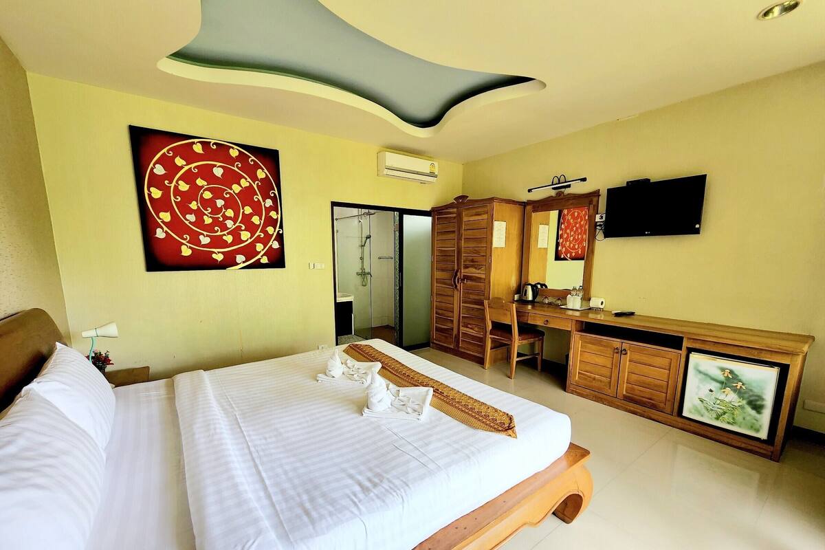 A hotel room with a large bed, a wooden desk, a mirror, and a television.