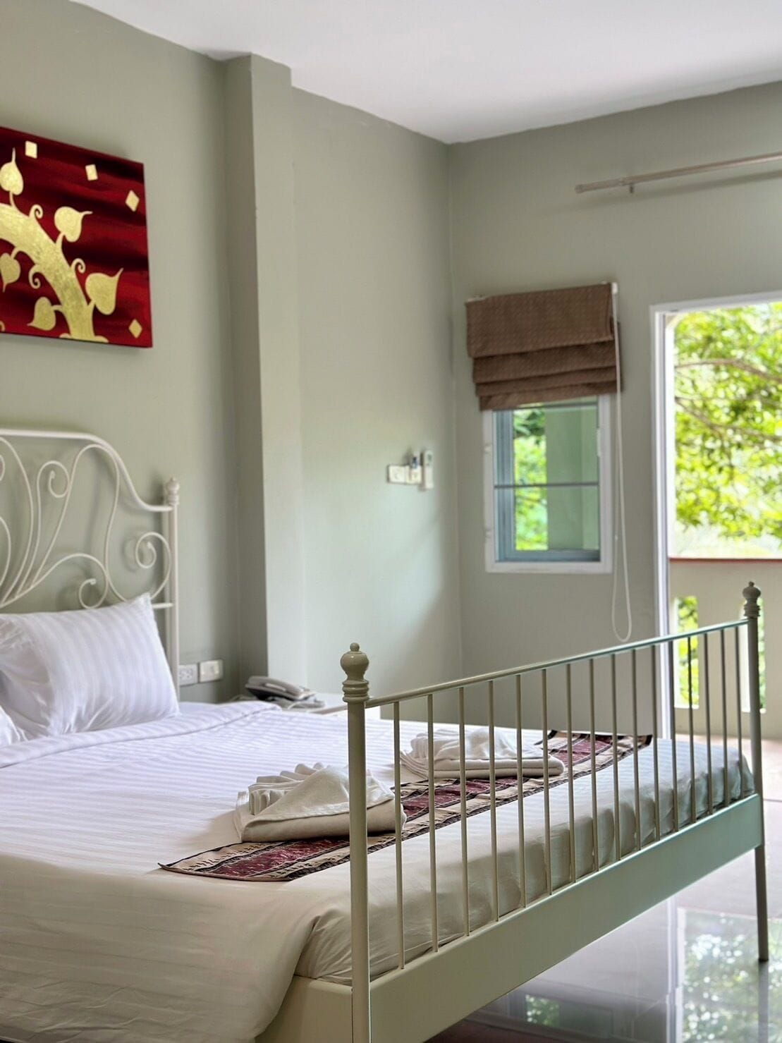 Un dormitorio con cama, mesita de noche, ventana con vistas y un cuadro decorativo en la pared.