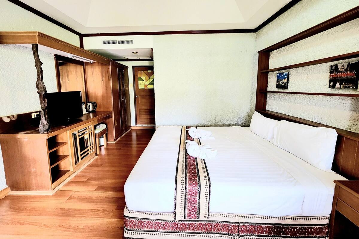 A hotel room with a large bed, wooden furniture, a television, and a small desk.