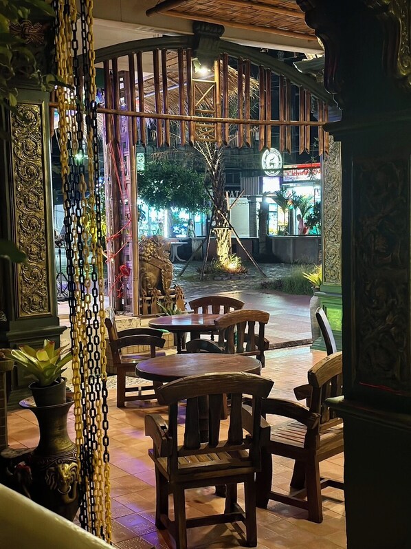 An indoor seating area with wooden tables and chairs, a decorative wall with intricate designs, and a view of the street outside. - Kata Garden Resort (Karon)