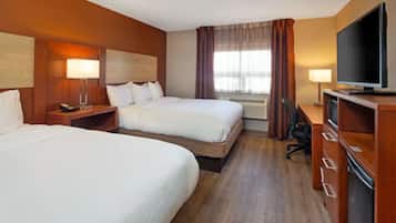 A hotel room with two beds, a television, a desk with a chair, and a window with curtains.