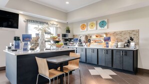 A modern kitchen with a central island, a dining area with two chairs, and a microwave. There are signs for 'Futfill Grains & Dairy' and 'Build Your Own'. - Best Western Auburndale Inn & Suites (Auburndale)