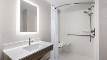 Un baño moderno con un lavamanos blanco, un espejo, una ducha con puerta de vidrio curvo y un mueble de tocador de madera.