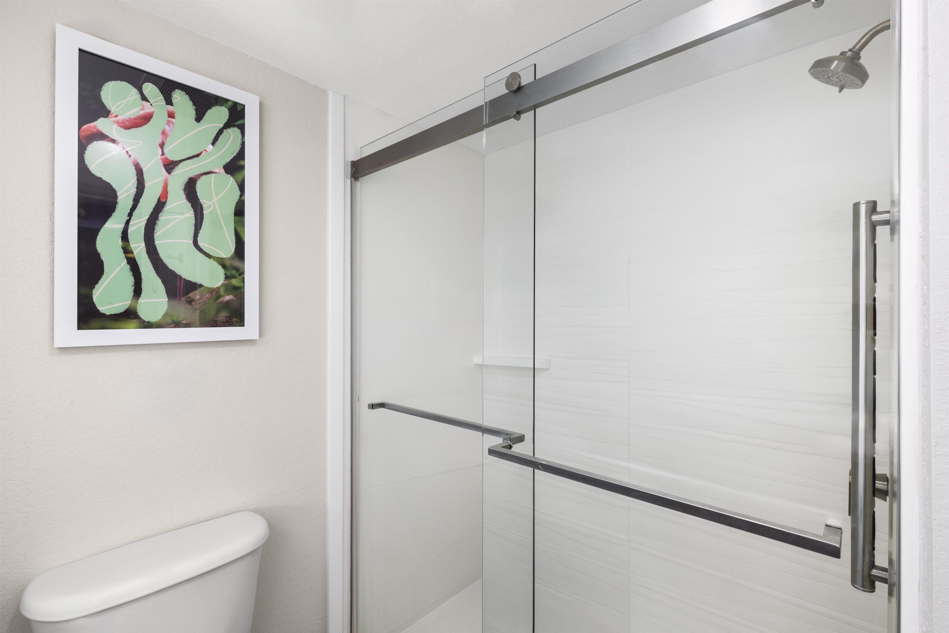A bathroom with a glass shower enclosure, a toilet, and a framed abstract painting on the wall.