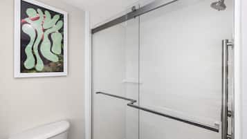 A bathroom with a glass shower enclosure, a toilet, and a framed abstract painting on the wall.