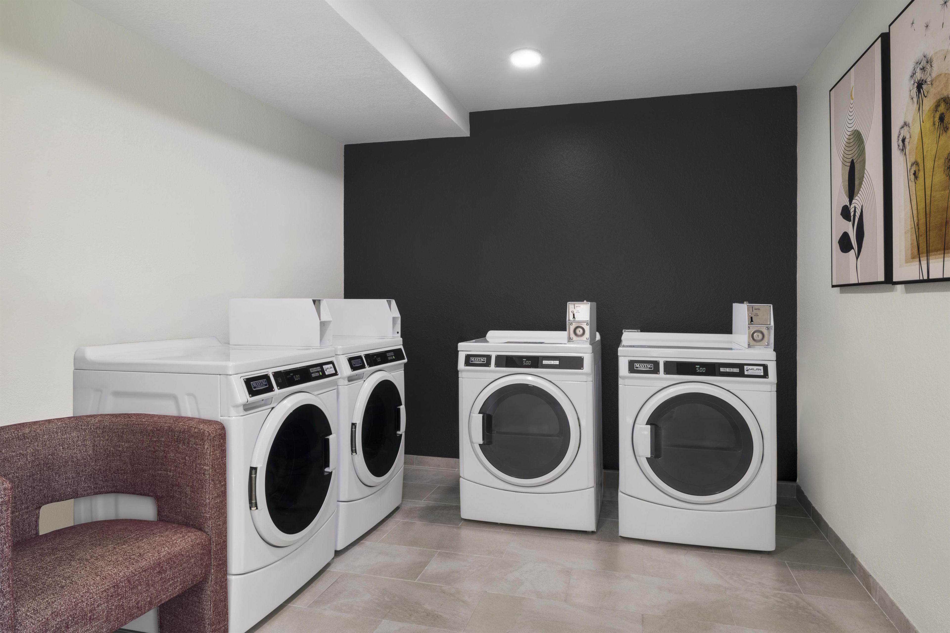 A laundry room with two front-loading washing machines, a dryer, and a chair.
