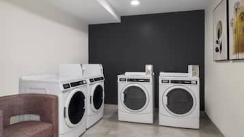 A laundry room with two front-loading washing machines, a dryer, and a chair.
