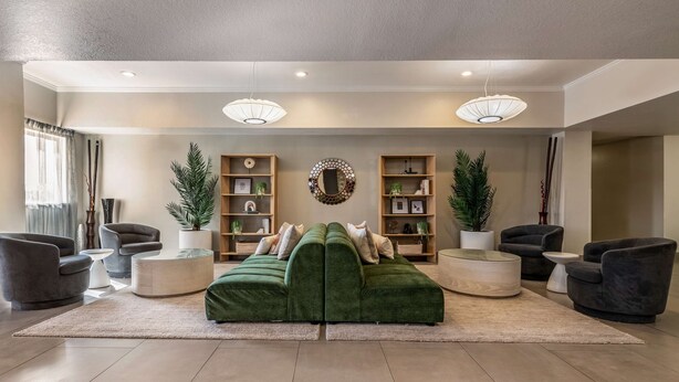 A modern living room with a green sectional sofa, two armchairs, a coffee table, and a bookshelf. - Best Western Auburndale Inn & Suites (Auburndale)