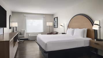 Una camera d'albergo con un letto grande, lampade ai comodini, una scrivania, una sedia, una televisione e una finestra con persiane.