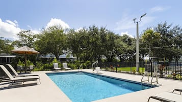 Una piscina rectangular con borde de azulejos, rodeada de sillas de descanso y una pequeña zona cubierta para sentarse.
