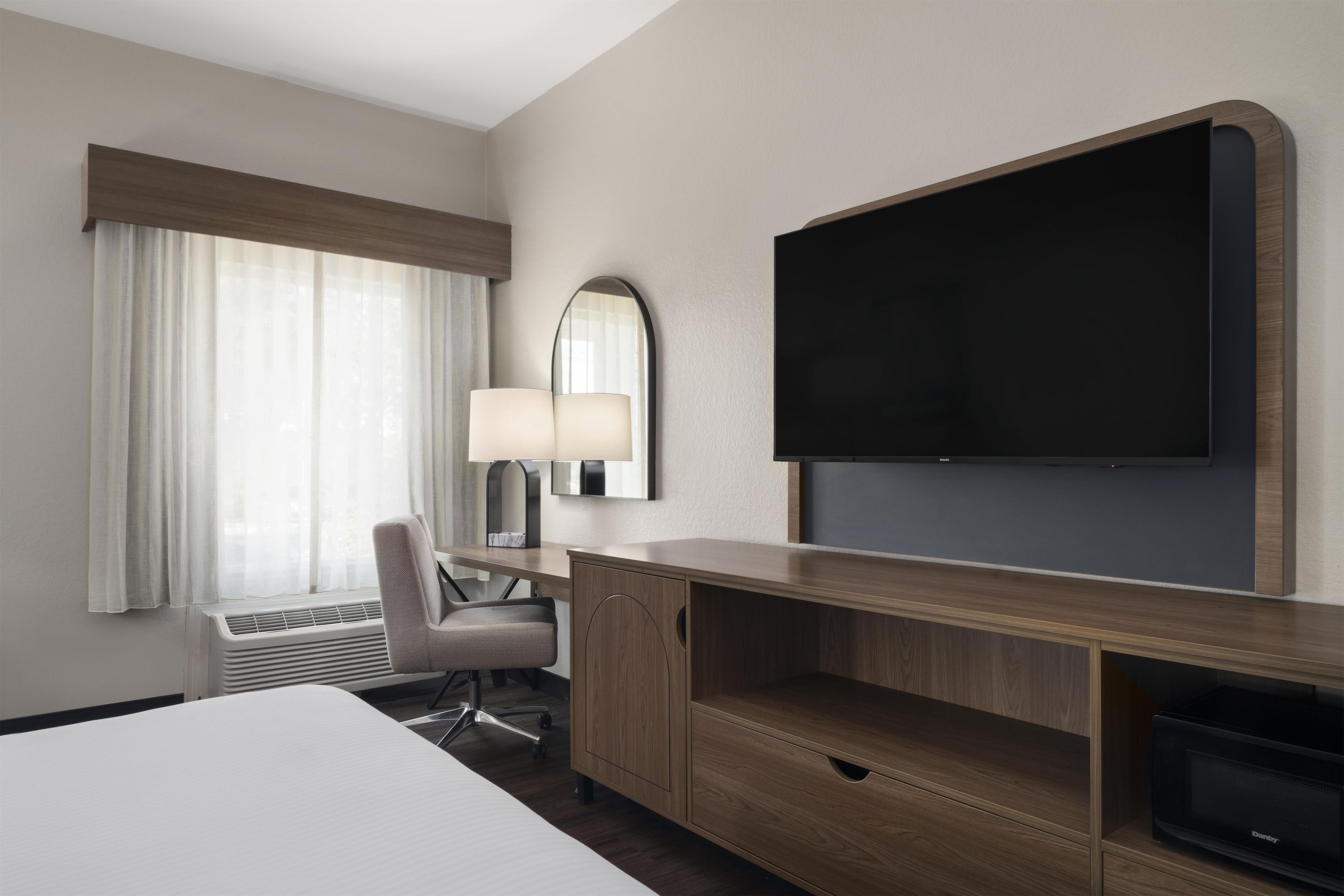 A hotel room with a bed, a desk with a lamp, a television, and a microwave.