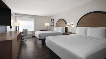 A hotel room with two beds, a desk, a chair, a TV, and a window.