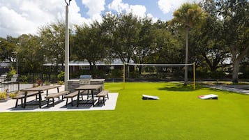 A park with picnic tables, a barbecue grill, and a volleyball net.