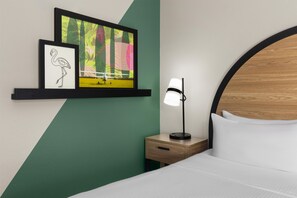 A hotel room with a bed, a nightstand with a lamp, a shelf with artwork, and a green accent wall. - Best Western Auburndale Inn & Suites (Auburndale)