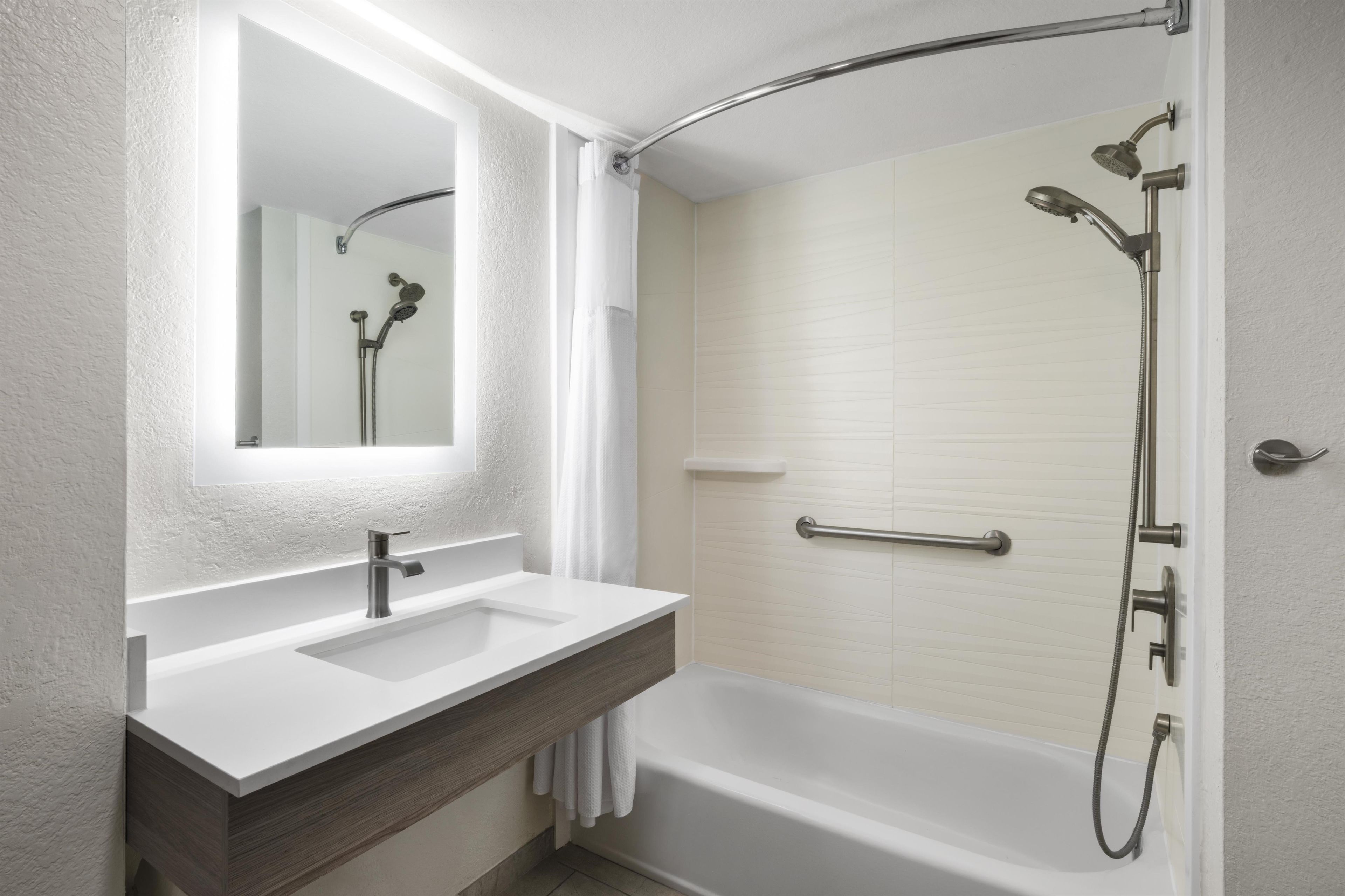 A modern bathroom with a white vanity, a large mirror, a bathtub, and a shower area.