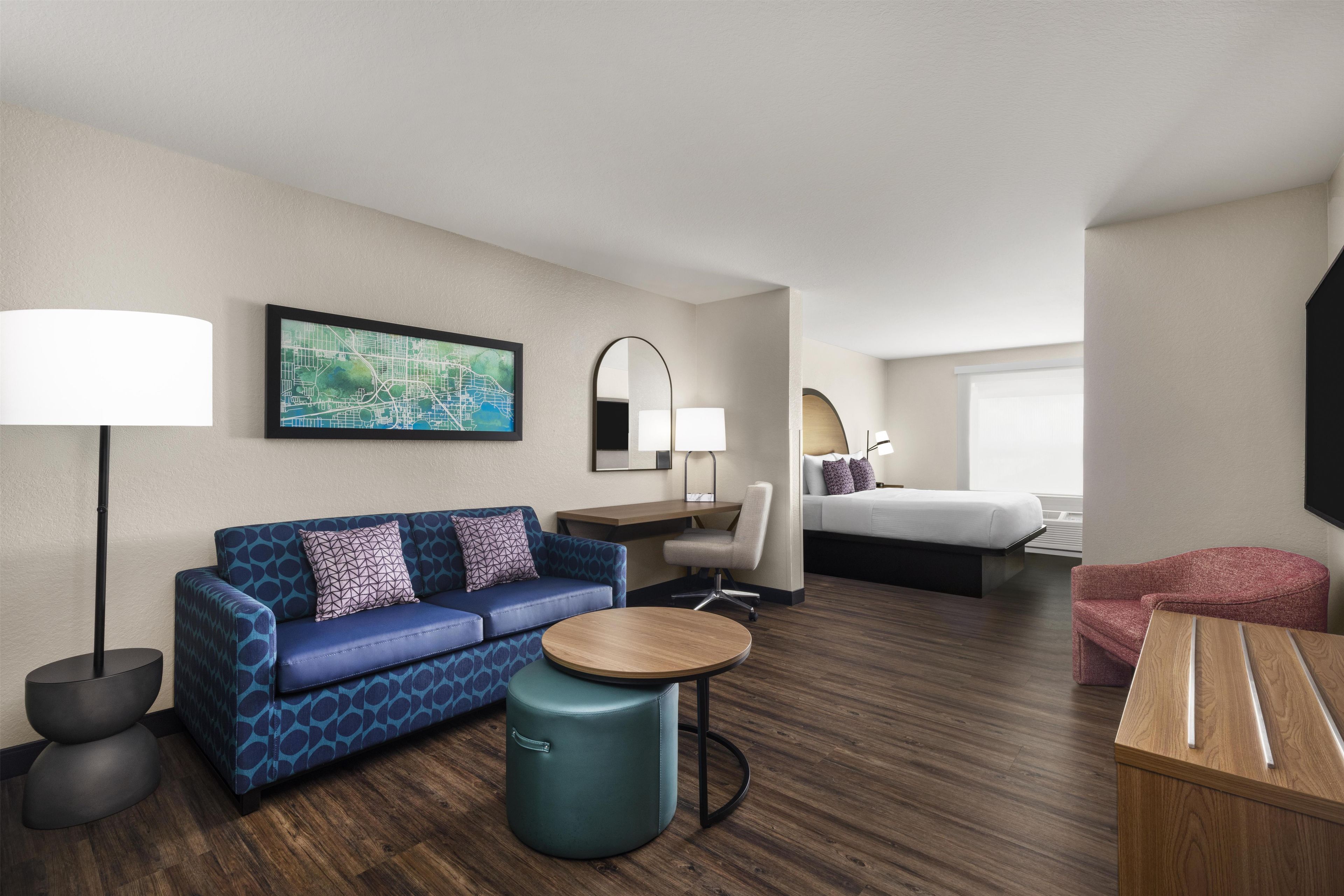 A hotel room with a blue sofa, a round wooden table, a bed, a desk, and a chair.