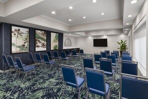 A conference room with rows of blue chairs, a flat-screen TV on the wall, and tropical leaf-patterned artwork on the walls. - Best Western Auburndale Inn & Suites (Auburndale)