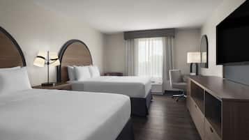 A hotel room with two beds, a desk, a chair, a TV, and a window with curtains.