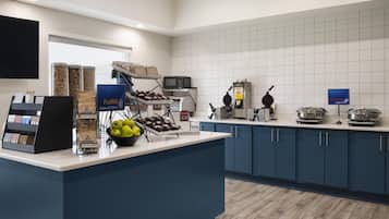 A self-service breakfast area with a variety of food options, including cereals, fruits, and a waffle maker.