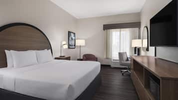 A hotel room with a large bed, a desk, a chair, a flat-screen TV, and a window with curtains.