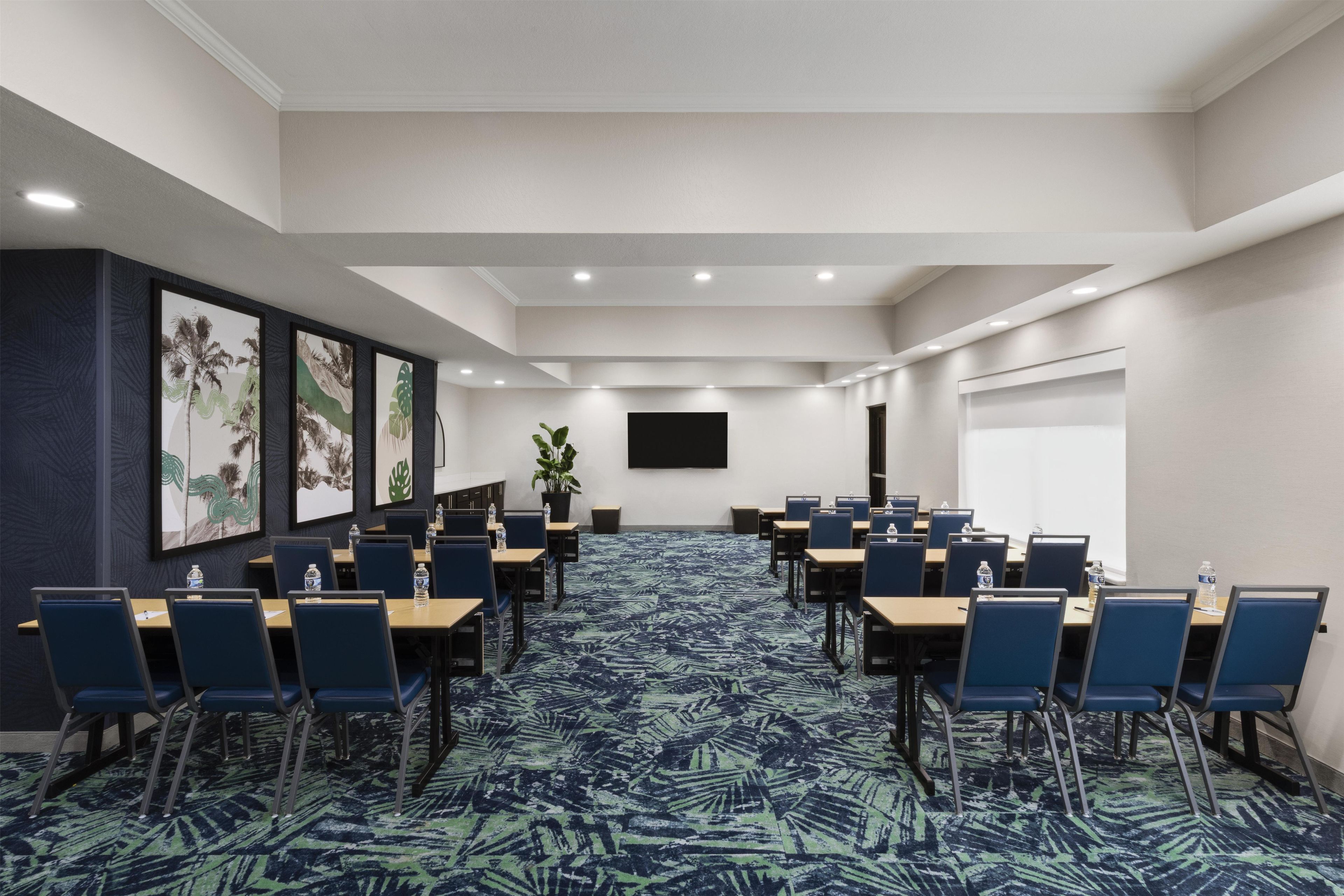 A conference room with a long table, chairs, a large screen, and framed artwork on the walls.