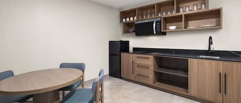 A compact kitchen with a dining table, chairs, a microwave, and a refrigerator.