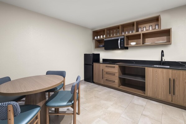 A compact kitchen with a dining table, chairs, a microwave, and a refrigerator. - Best Western Auburndale Inn & Suites (Auburndale)