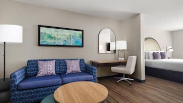 Habitación de hotel con un sofá azul, una mesa redonda de madera, un escritorio con una lámpara, una cama y un mapa grande en la pared.