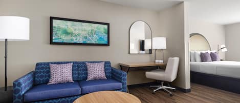 Quarto de hotel com um sofá azul, uma mesa redonda de madeira, uma escrivaninha com abajur, uma cama e um mapa grande na parede.