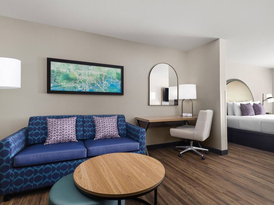 Habitación de hotel con un sofá azul, una mesa redonda de madera, un escritorio con una lámpara, una cama y un mapa grande en la pared.