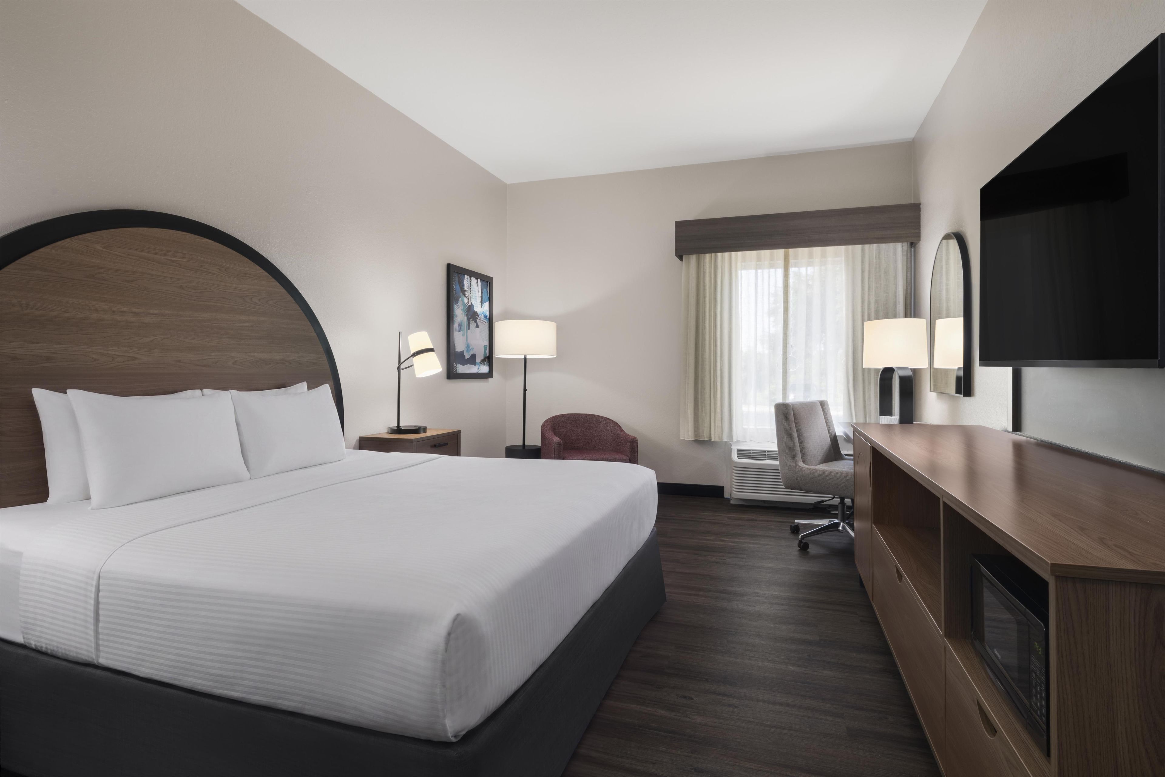 A hotel room with a large bed, a desk, a chair, a flat-screen TV, and a window with curtains.