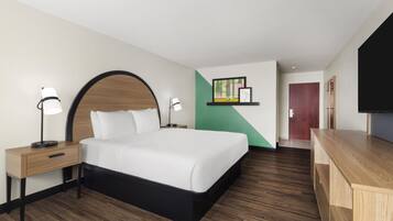 A hotel room with a bed, bedside tables, a desk, a chair, a television, and artwork on the wall.