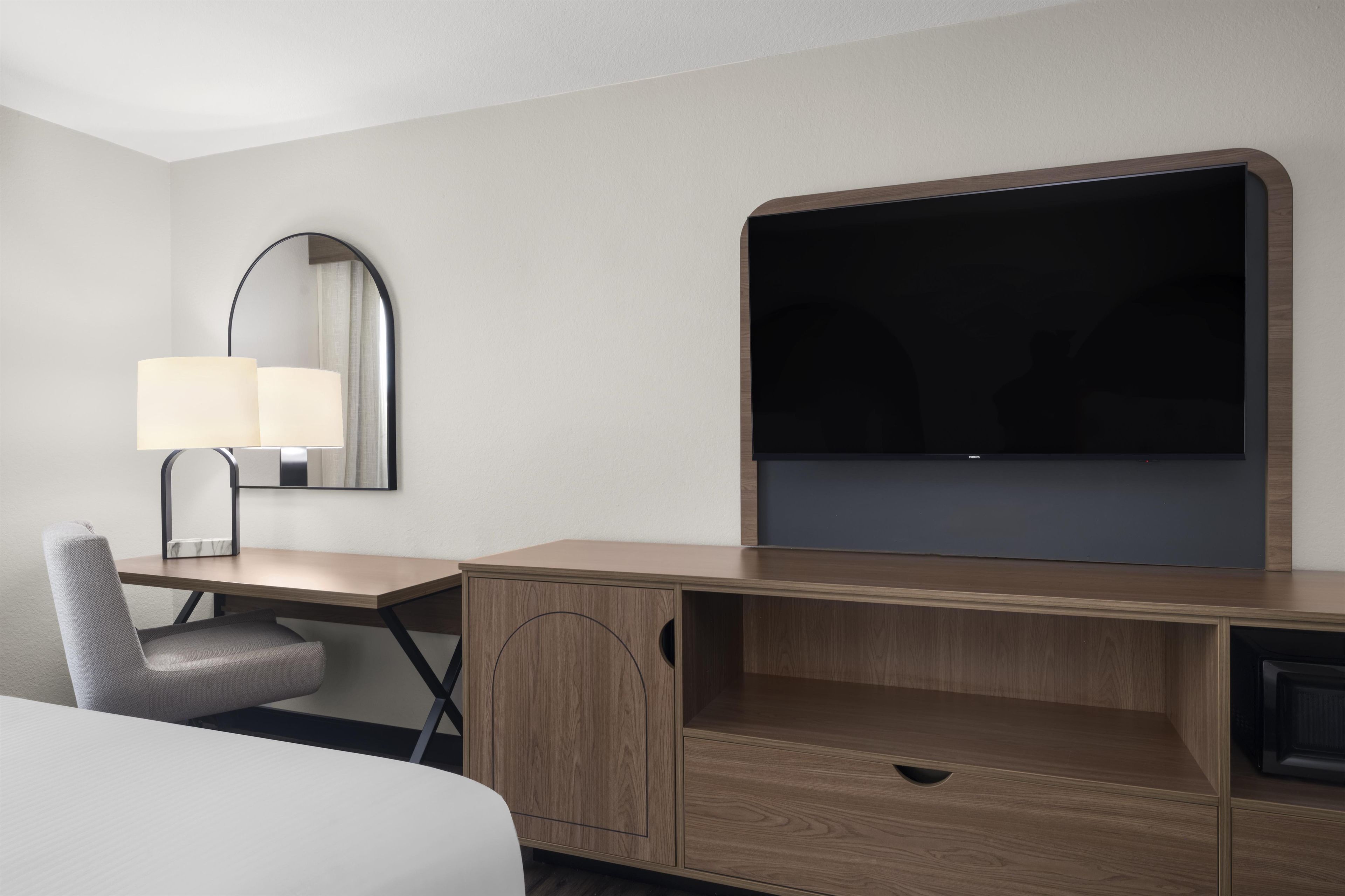 Une chambre d’hôtel avec un bureau en bois, une chaise, un lit, un téléviseur à écran plat et un miroir.