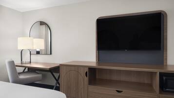 Une chambre d’hôtel avec un bureau en bois, une chaise, un lit, un téléviseur à écran plat et un miroir.