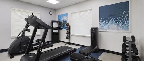 A gym with a treadmill, bench, dumbbells, and a water dispenser.