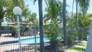 A fenced outdoor area with a pool, palm trees, and a gazebo. - Country Road Motel (Queenton)