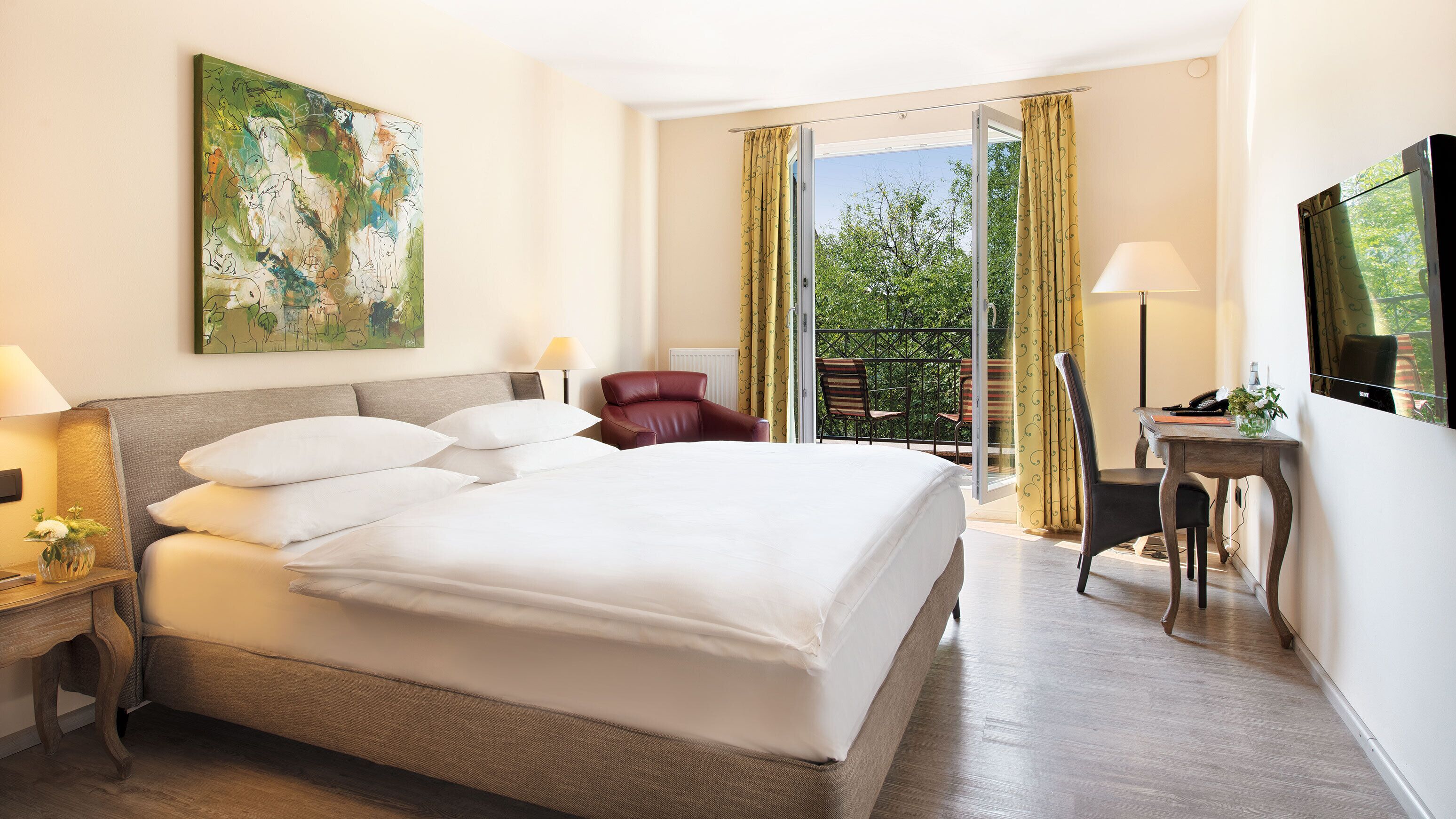 Habitación de hotel con una cama grande, un escritorio, una silla, un televisor y un balcón con cortinas.