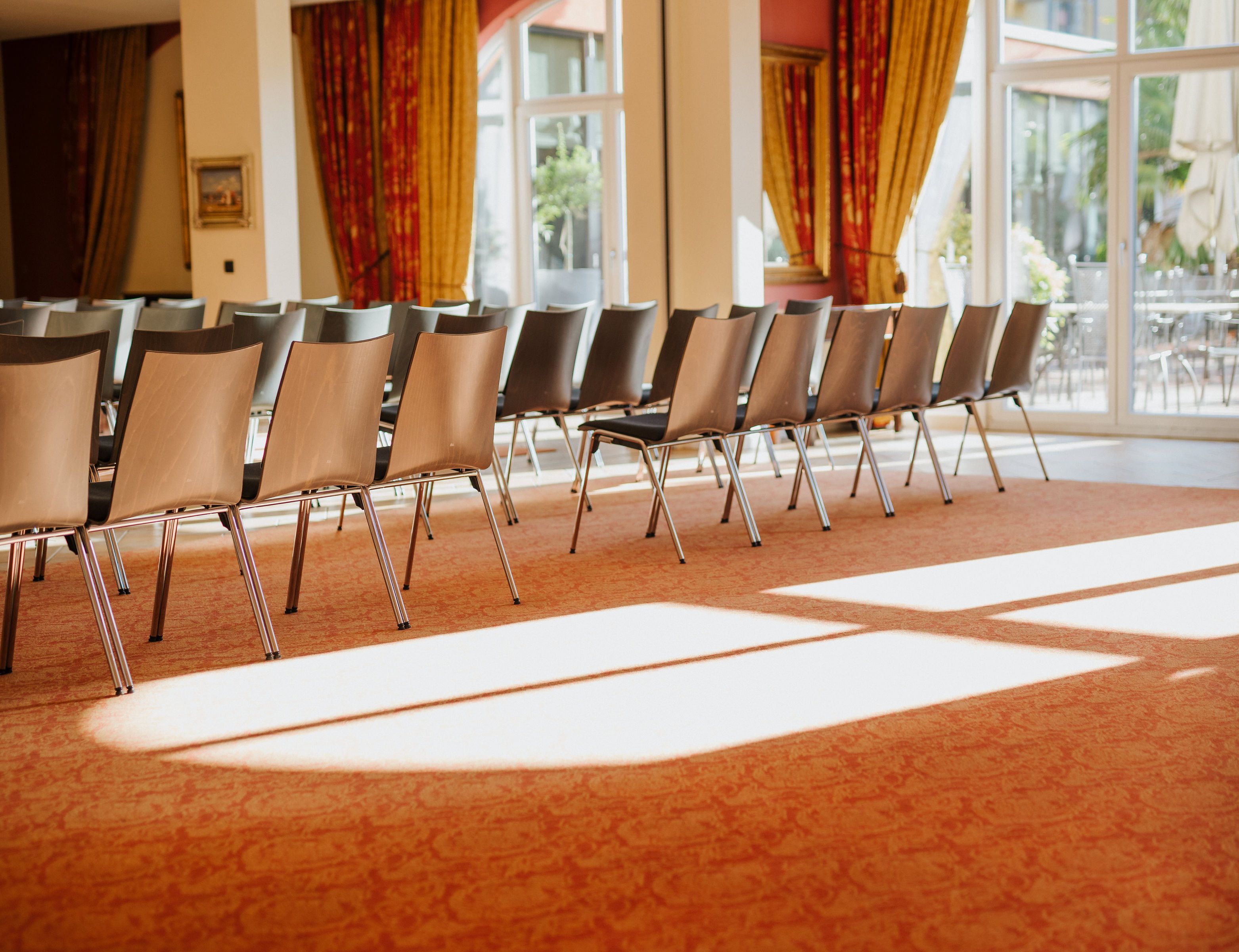 Rows of chairs arranged in a conference room with a patterned carpet and large windows with curtains.