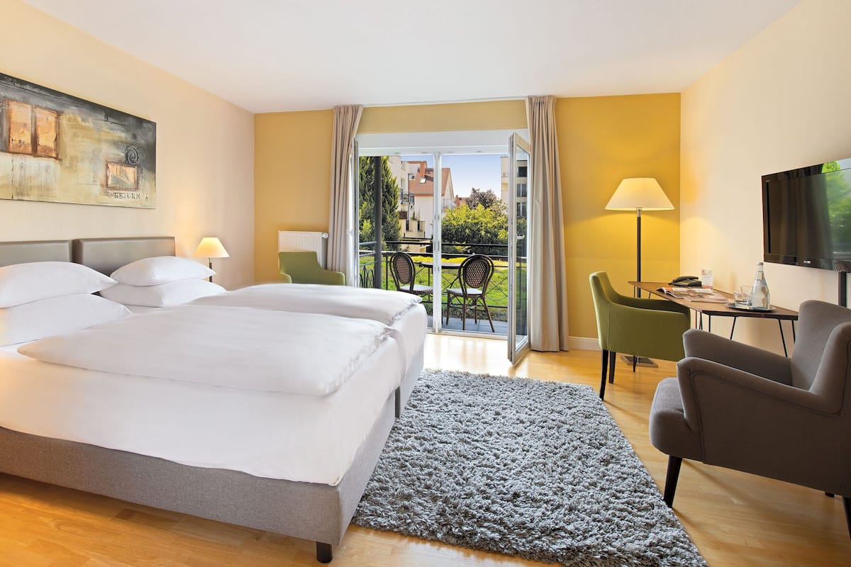 Une chambre d’hôtel avec un lit double, un bureau avec une chaise, une télévision et un balcon offrant une vue sur la ville.