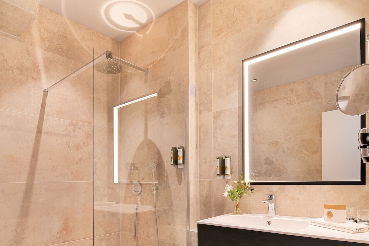 Une salle de bain moderne dotée d’une douche à parois de verre, d’un grand miroir et d’un meuble-lavabo avec un évier et un porte-serviettes.