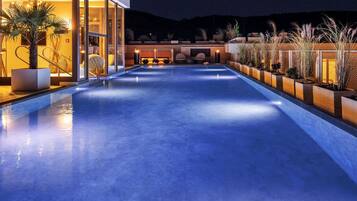 Ein Pool mit modernem Design, umgeben von Topfpflanzen und einem gut beleuchteten Außenbereich.