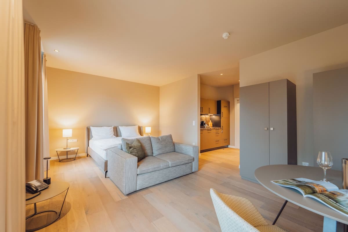 Une chambre d’hôtel moderne avec un lit, un canapé, une table à manger et un coin cuisine à l’arrière-plan.